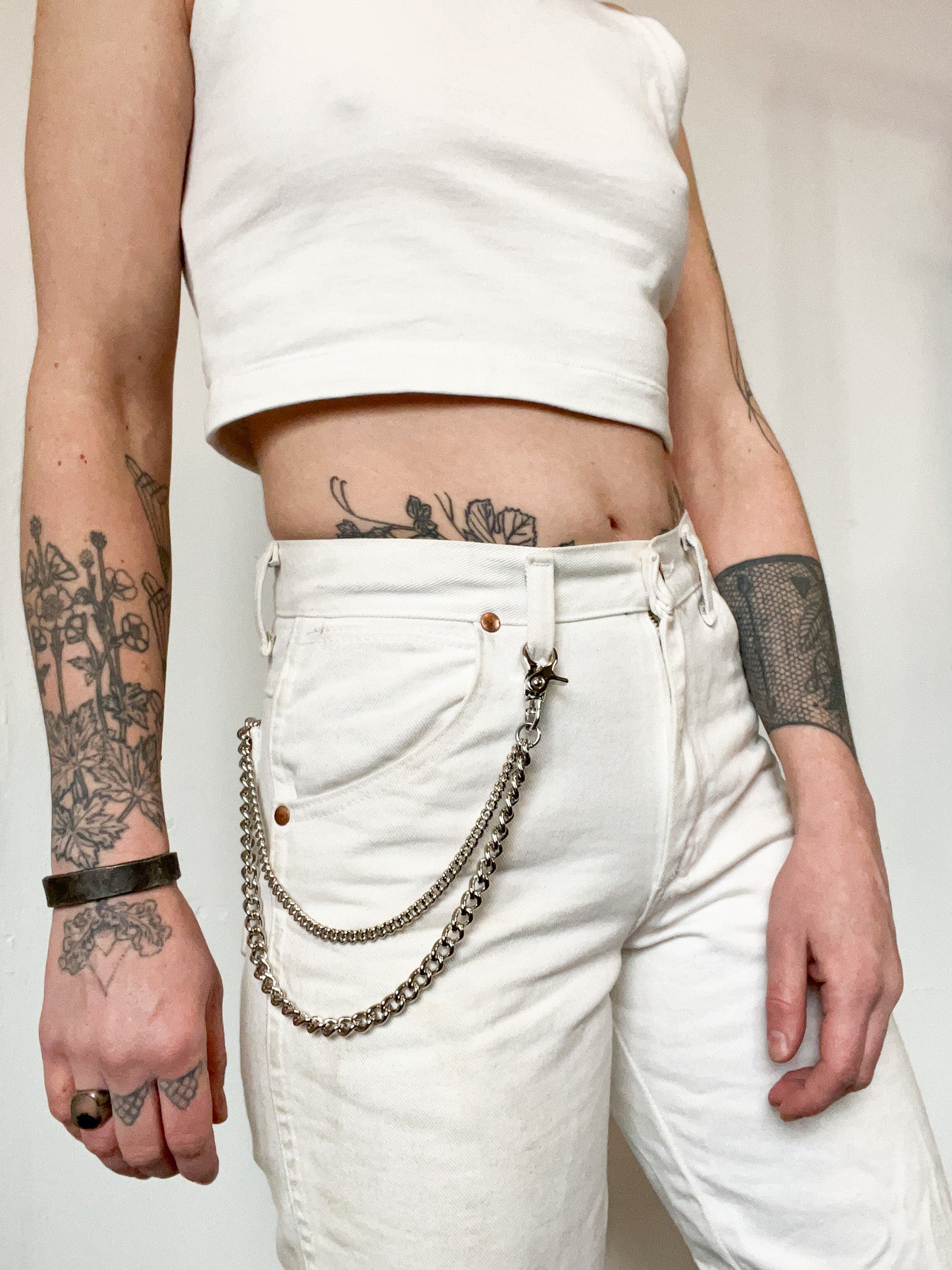 Tattooed person stands with hands at sides wearing an all white outfit and an agate chain in stainless steel. The agate chain is a double wallet chain with one larger curb chain of 1/4" and a small curb chain of 3/8"